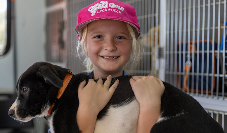 A young blonde child in a pink hat holds and adoptable puppy inside the adoption truck
